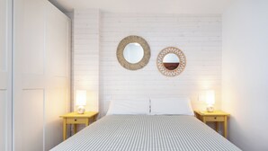 Un dormitorio ordenado con una colcha a cuadros, dos mesitas de noche con lámparas y dos espejos en la pared.