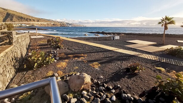 Un paseo marítimo con sendero rocoso, zonas de muelle de madera y vista al mar.