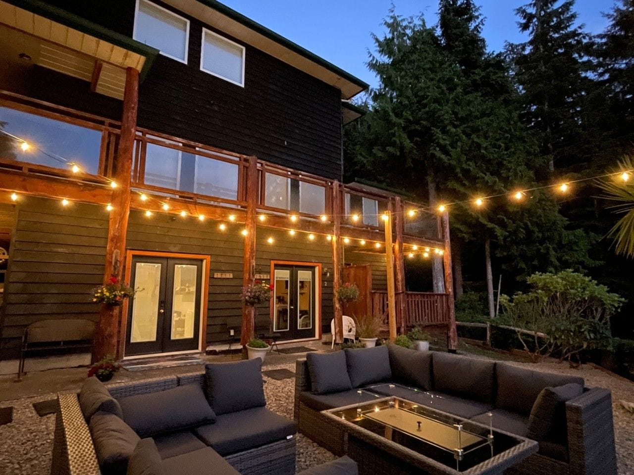 A wooden house with a porch, outdoor seating, and string lights.