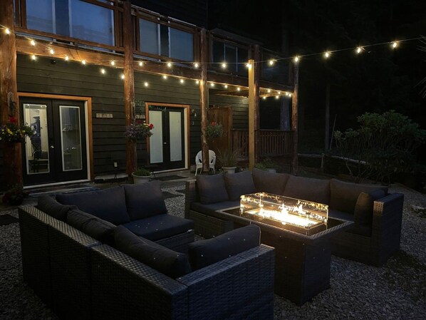 An outdoor seating area with a fire feature, surrounded by a wooden deck and string lights.