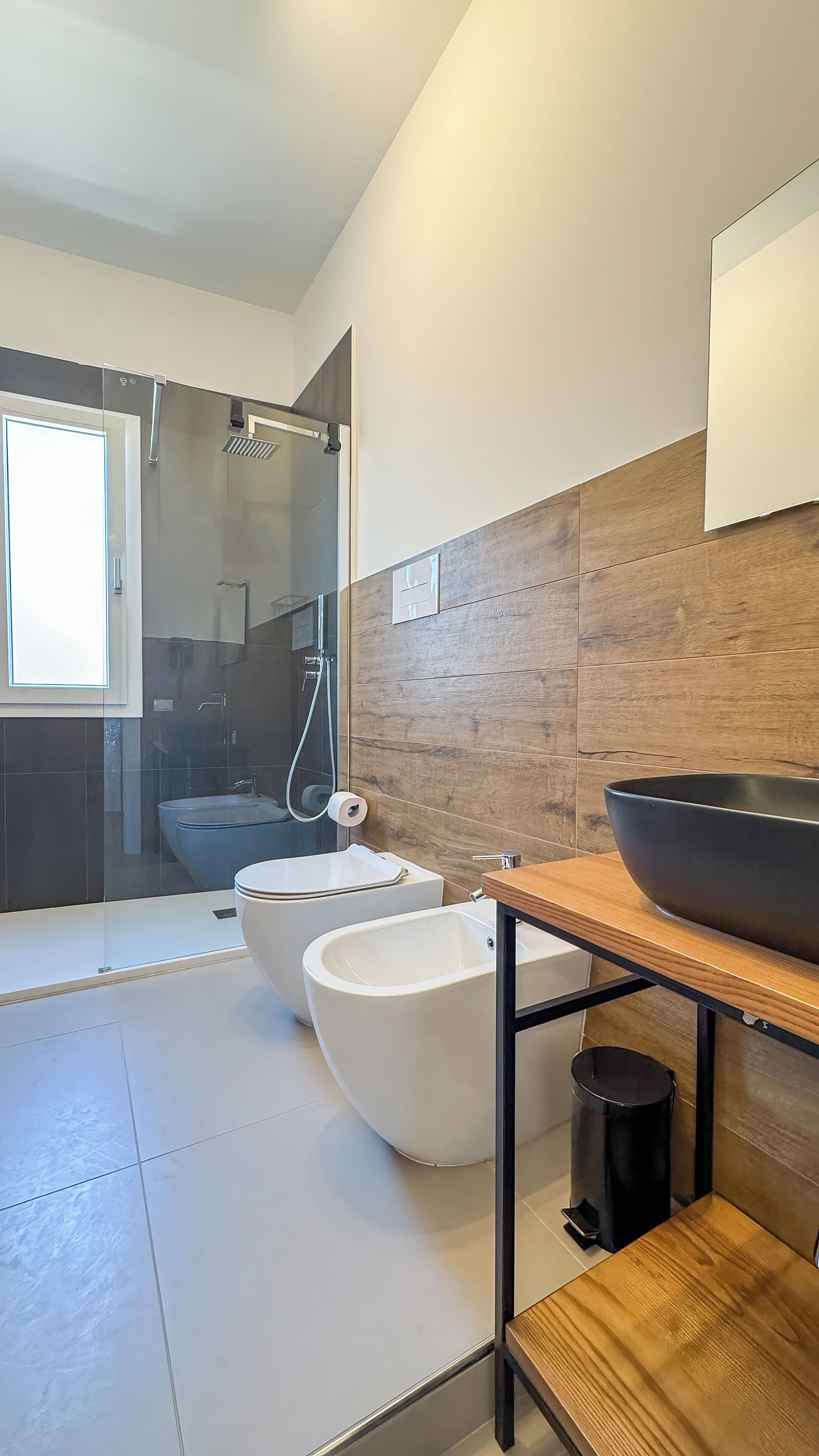 Un baño moderno con ducha, bidé, inodoro y un mueble de tocador de madera con lavabo.