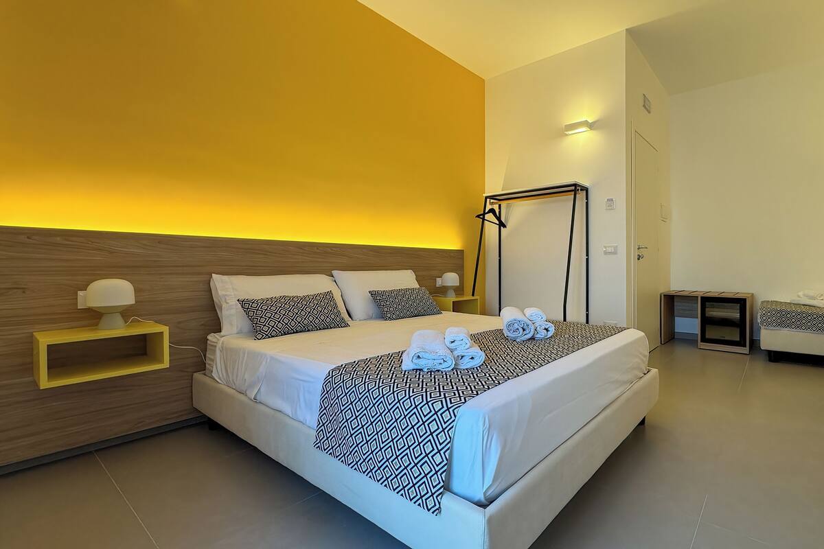 A modern hotel room with a large bed, bedside tables, a wardrobe, and a bathroom.