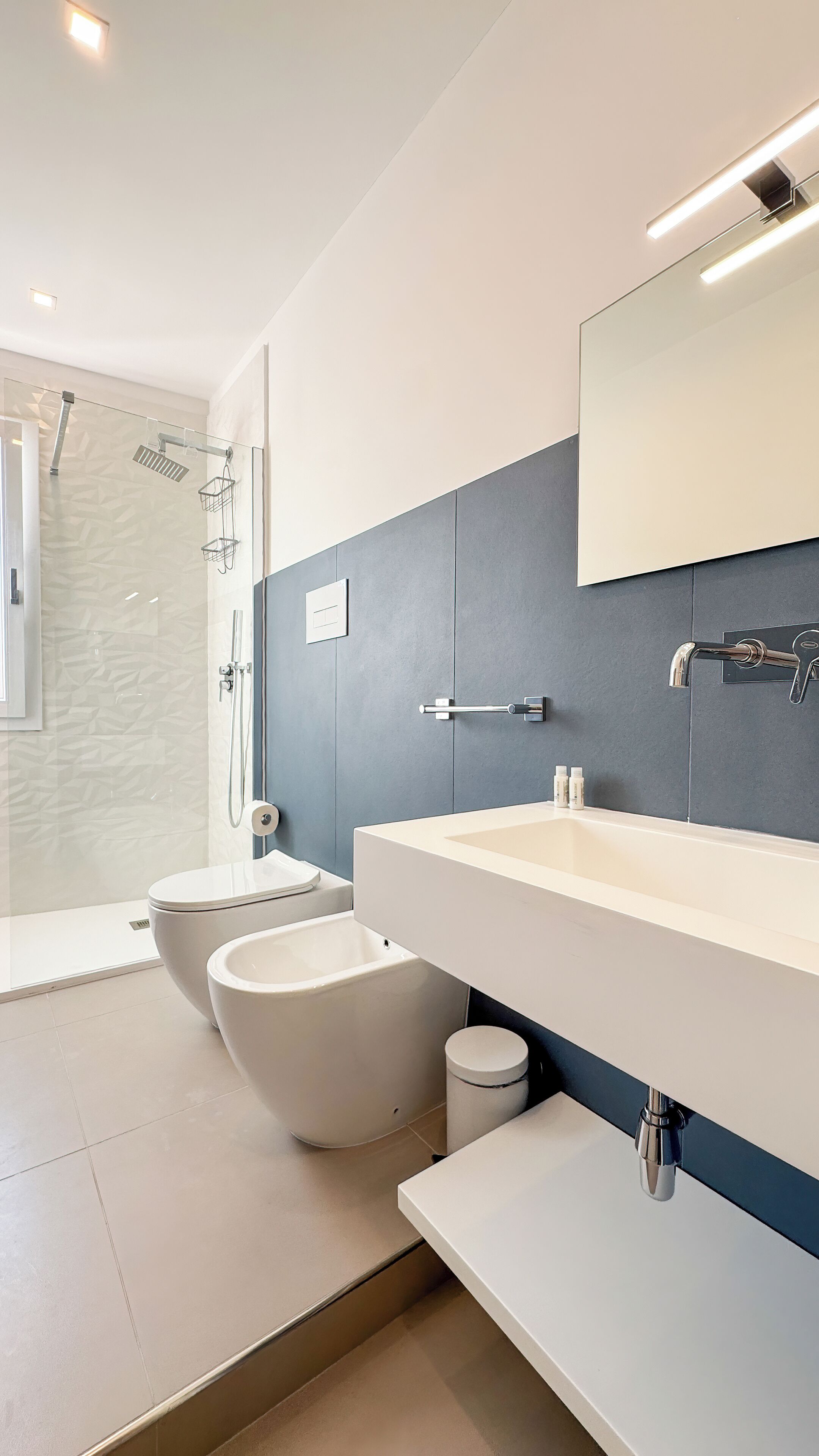 A modern bathroom with a glass shower enclosure, a white toilet, and a large sink with a mirror above it.