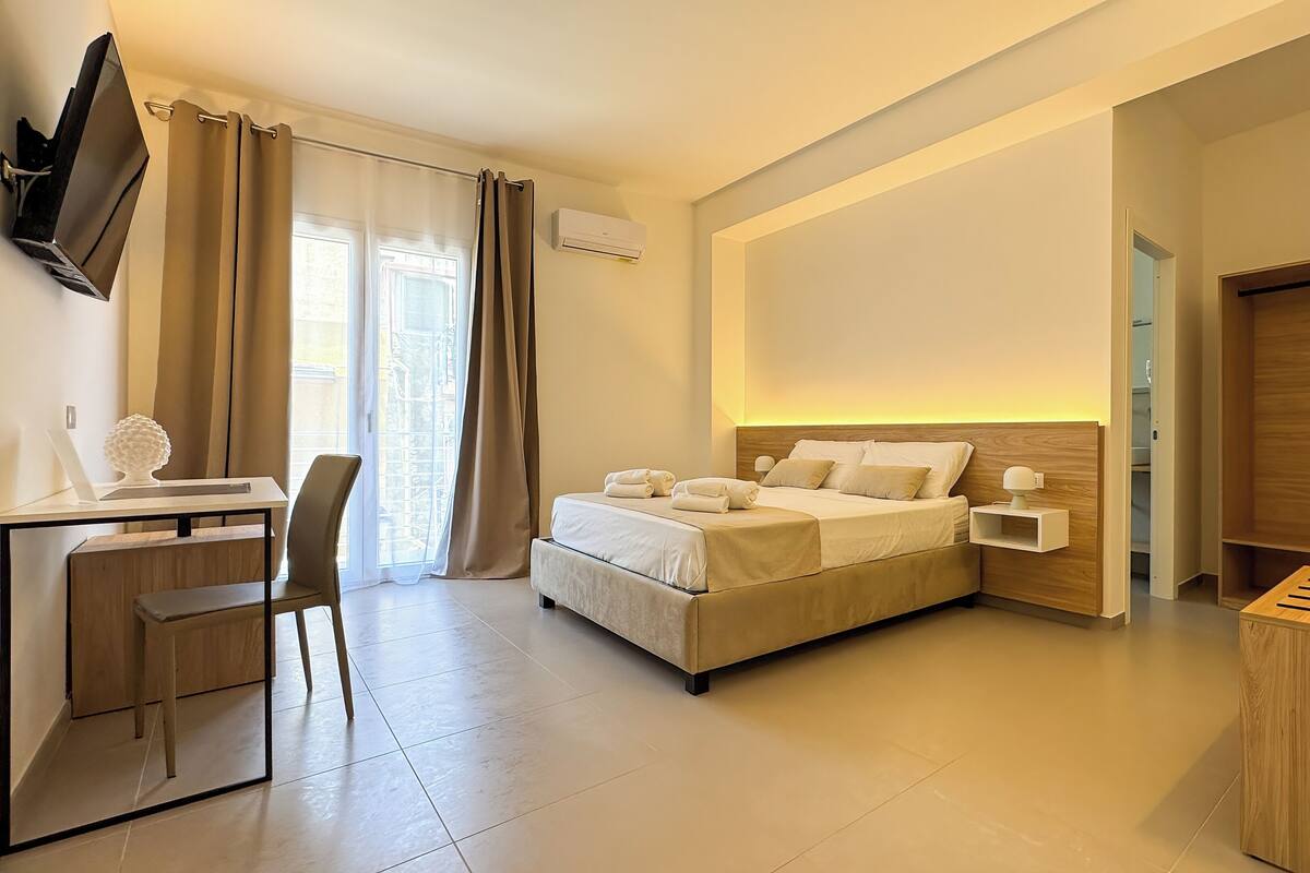 A modern hotel room with a bed, desk, chair, and a TV mounted on the wall.