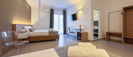 A modern hotel room with a large bed, a desk, a chair, a TV, and a wardrobe.