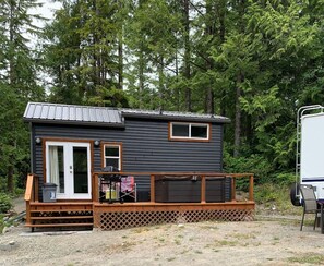 A small cabin with a deck, a door, and a window. - Tranquil Tiny Home/Ucluelet/Ocean - BBQ & hot tub (Alberni Clayoquot Regional District)