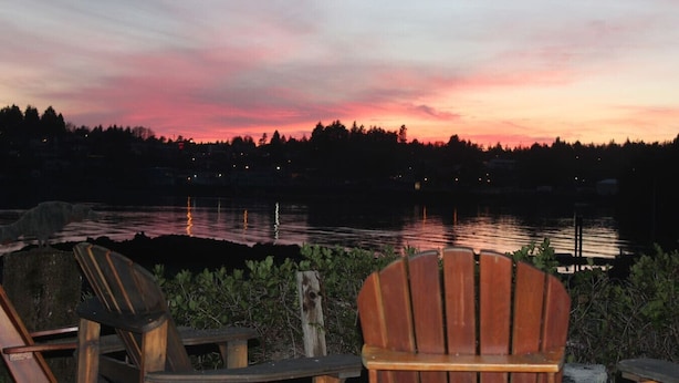 A wooden chair facing a body of water with a sunset in the background. - Ucluelet/Ocean/Treehouse Cabin - hot tub, kitchen, deck, Roku TV (Alberni Clayoquot Regional District)