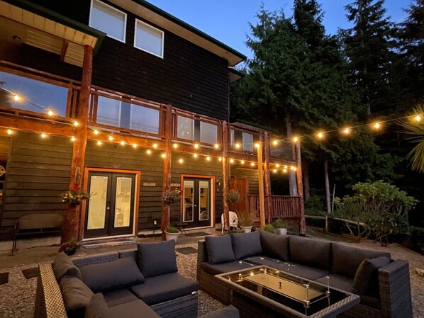 Una casa de madera con porche, mobiliario exterior e iluminación de luces colgantes.