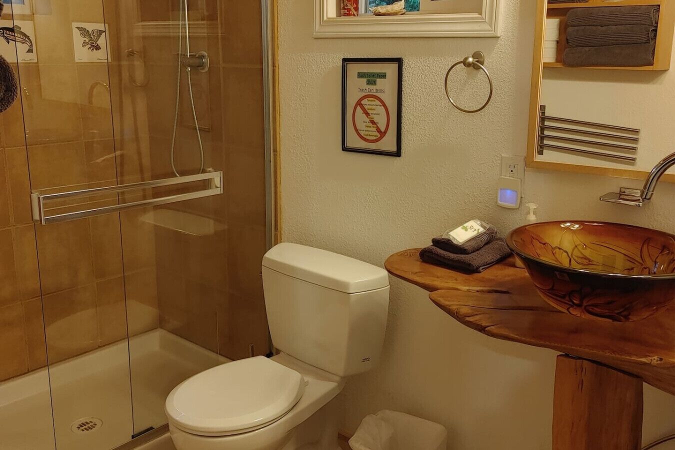 Ein Badezimmer mit einer Duschkabine, einer weißen Toilette und einem hölzernen Waschtisch mit einer Glasbeckenwaschschale.