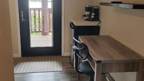 A small room with a wooden table, a chair, a coffee maker, and a TV on a shelf.