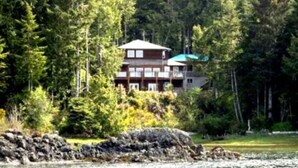 A multi-story building with a green roof, surrounded by dense forest.