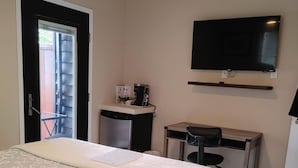 A hotel room with a bed, a desk with a chair, a television mounted on the wall, and a coffee machine on the desk.