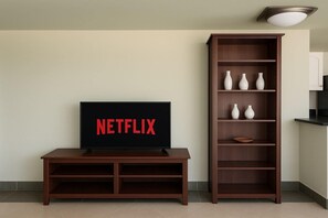 A living room with a TV displaying the Netflix logo, a wooden entertainment center, and a tall bookshelf with vases. - 2114 · Rooftop 1BDR | Terrace | 2 BA (New Cairo City)