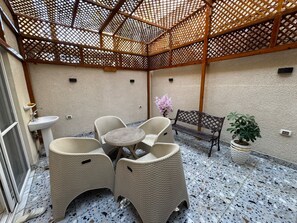 Ein überdachter Patio-Bereich mit Tisch, Stühlen, einer Bank, einem Blumentopf und einem Waschbecken.