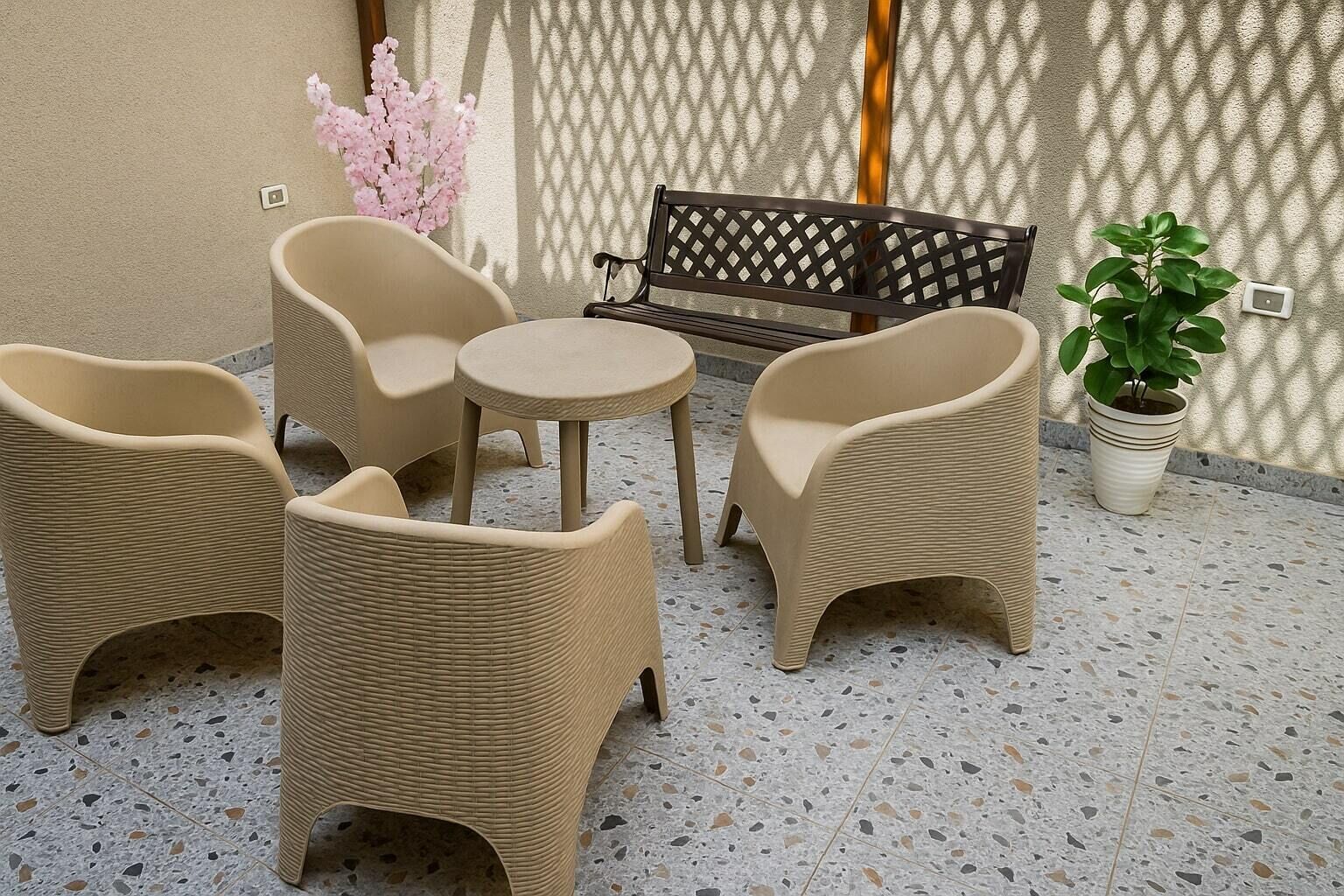 A patio with wicker furniture, including chairs and a small table, a bench, and a potted plant.