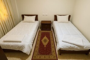 Ein Zimmer mit zwei Einzelbetten, einem kleinen Nachttisch aus Holz und einem Teppich mit rotem und goldenem Muster.