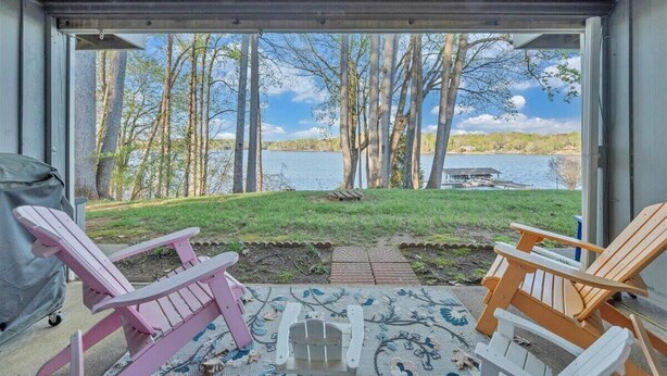 Une véranda couverte avec des fauteuils Adirondack, un barbecue et une vue sur un lac et des arbres.