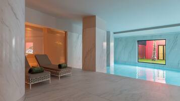 Un espace piscine intérieur moderne, doté d’un sol en marbre, de deux chaises longues et offrant une vue sur une pièce aux couleurs rouge et jaune, grâce à un mur de verre.