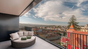 Un balcón con una zona de estar circular, vistas a un paisaje urbano y un edificio con un tejado rojo característico.
