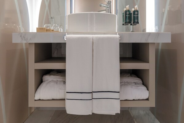 A bathroom with a marble sink, two shelves with folded towels, and a mirror above the sink.