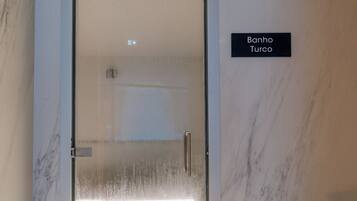Un bagno con porta in vetro, un corrimano e un cartello con la scritta 'Banho Turco'.