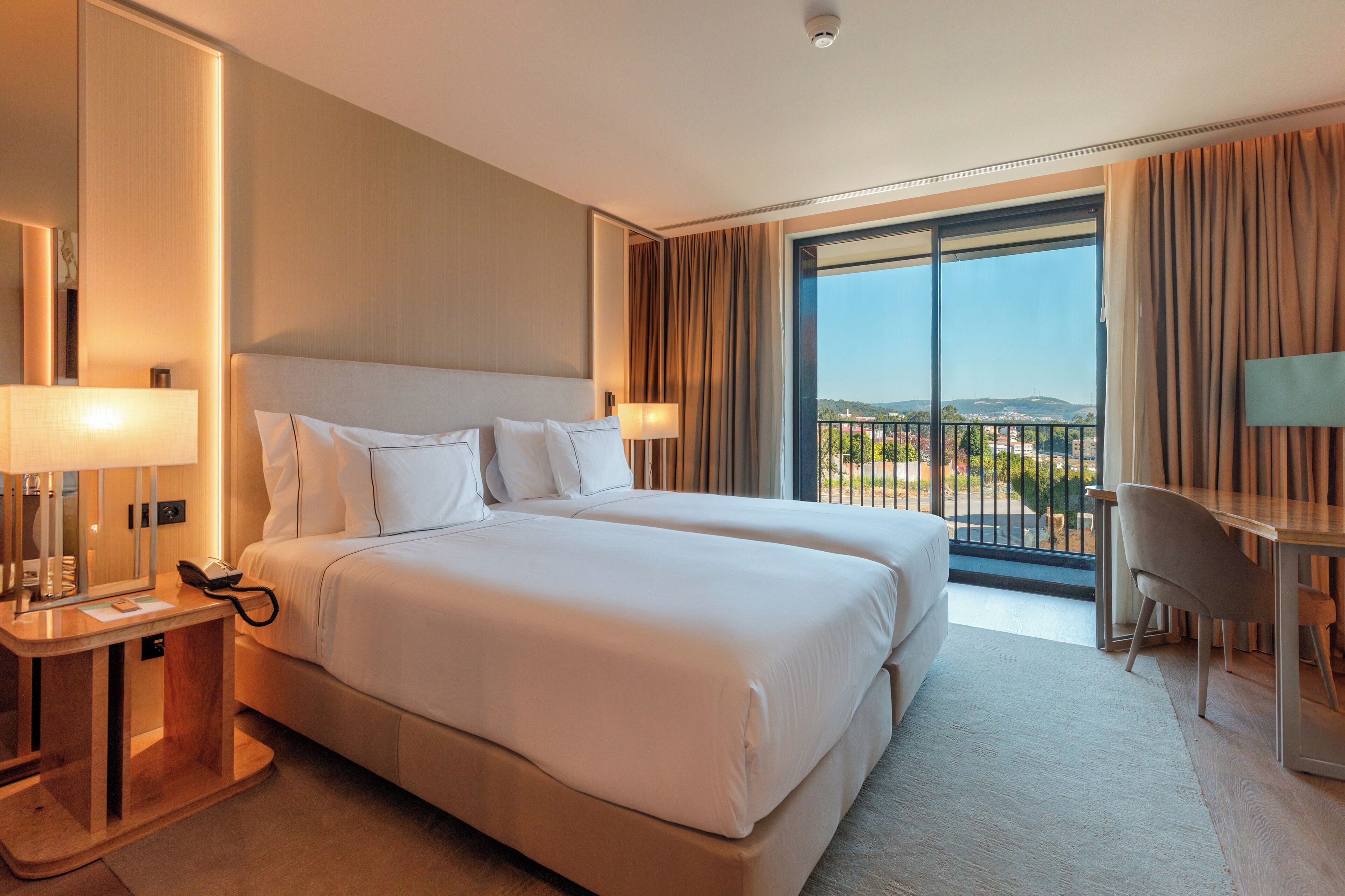 Ein Hotelzimmer mit zwei Betten, einem Schreibtisch, einem Sessel, einem Fernseher und einem Balkon mit Blick.