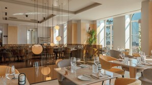 Un restaurante moderno con un separador de vidrio, mesas dispuestas con cubiertos e iluminación colgante.