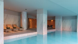 Una piscina interior moderna con paredes de mármol y sillones de descanso.