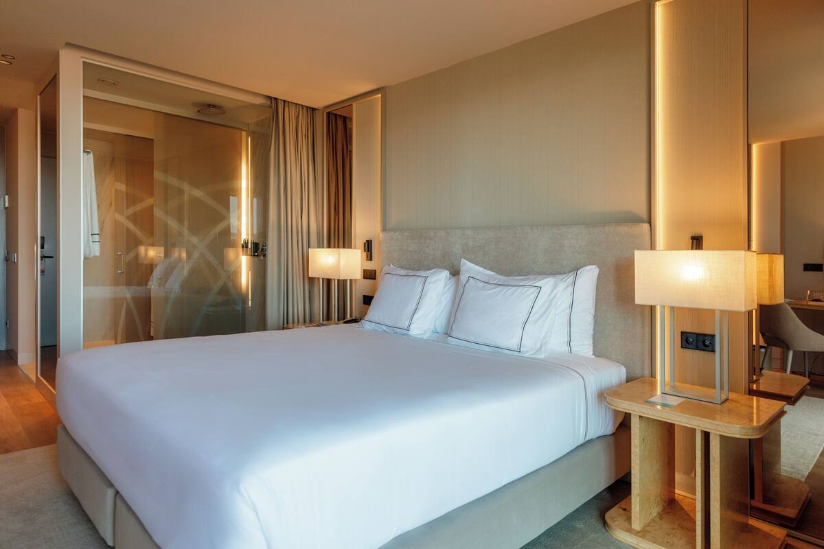 A hotel room with a large bed, bedside lamps, a mirror, and a door leading to a bathroom.