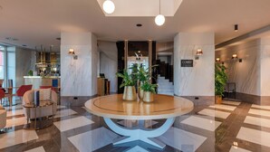 Un vestíbulo con una mesa redonda, plantas en macetas, una zona de bar y una escalera.