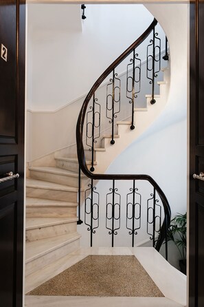 Una escalera de caracol con barandilla metálica, alfombra color beige y una planta en maceta.