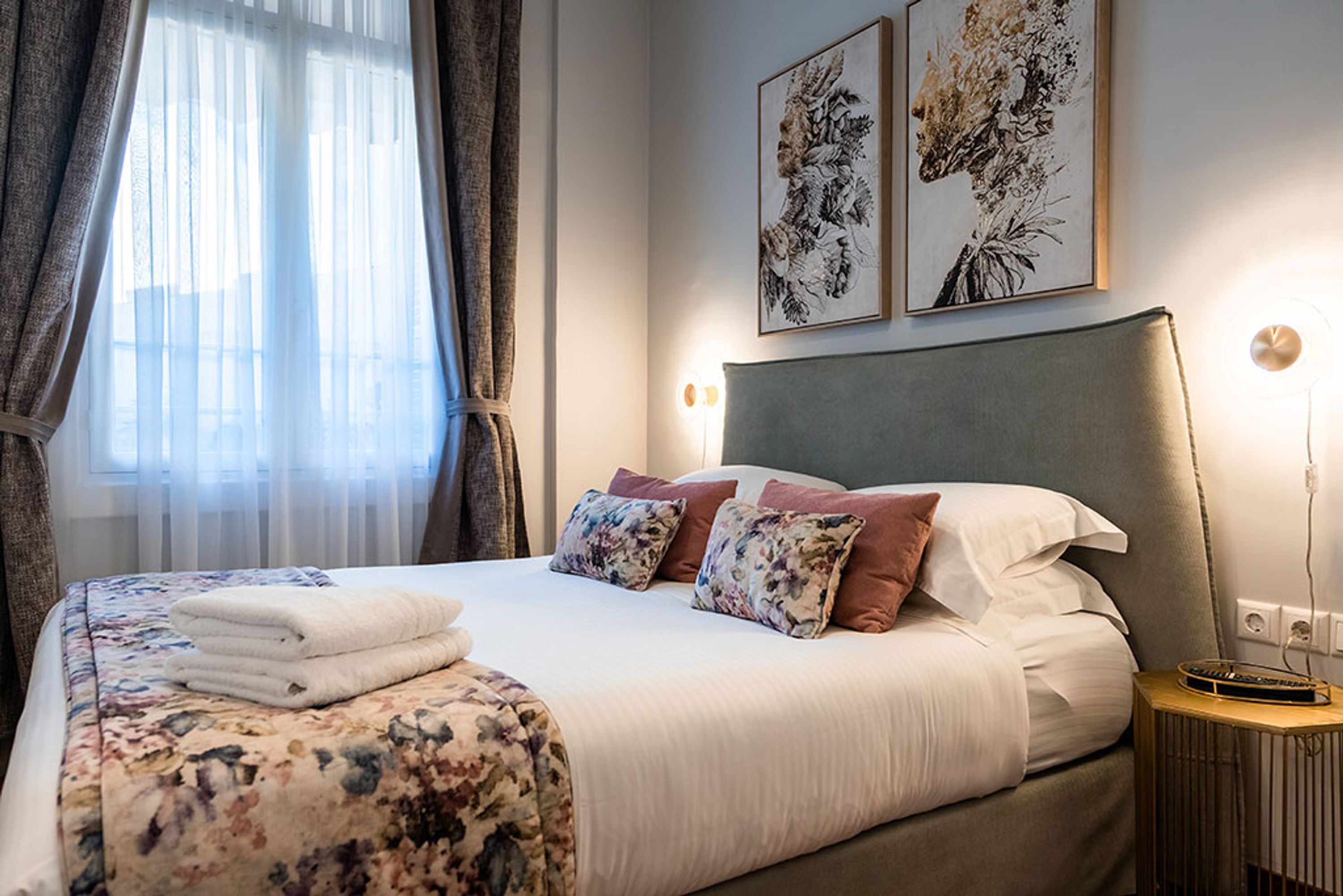 A neatly made bed with floral bedding, a headboard, and two wall-mounted artworks.