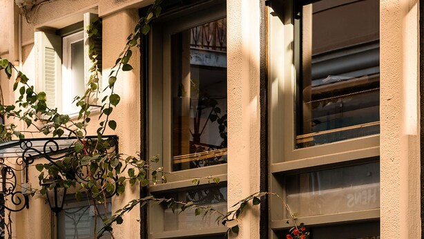 A bench outside a building with a door and window, potted plants, and a wall-mounted light fixture. - Asty Luxury Apartments (Athens)