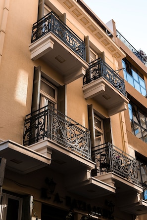 A building with multiple balconies featuring ornate black railings, a beige facade, and a sign indicating a hotel. - Asty Luxury Apartments (Athens)