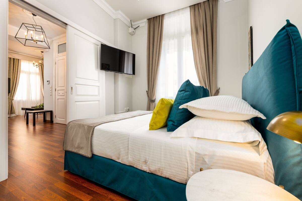 A bedroom with a bed, a TV mounted on the wall, and a window with curtains.