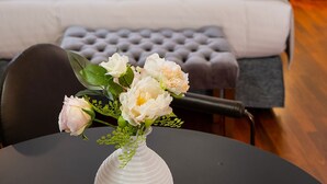 A bedroom with a bed, pillows, a bedside table, and a vase with flowers on a table. - Asty Luxury Apartments (Athens)