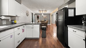 A modern kitchen with white cabinets, a black refrigerator, and a wooden floor. - 4 bedroom house WiFi/AC/deck/firepit/grill Laurel Lake/Cumberland Falls, Corbin (Corbin)