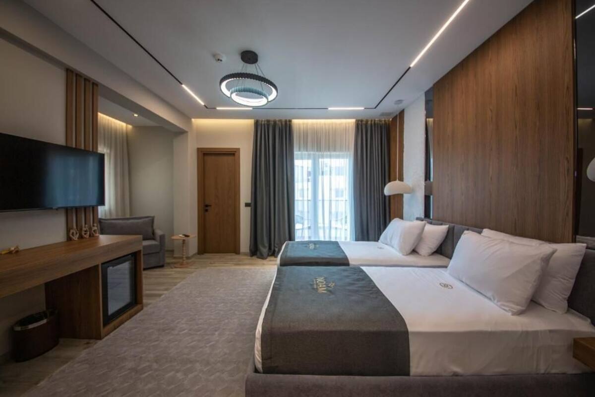 Habitació d'hotel moderna amb dos llits, televisió de pantalla plana, escriptori de fusta i una finestra gran amb cortines.