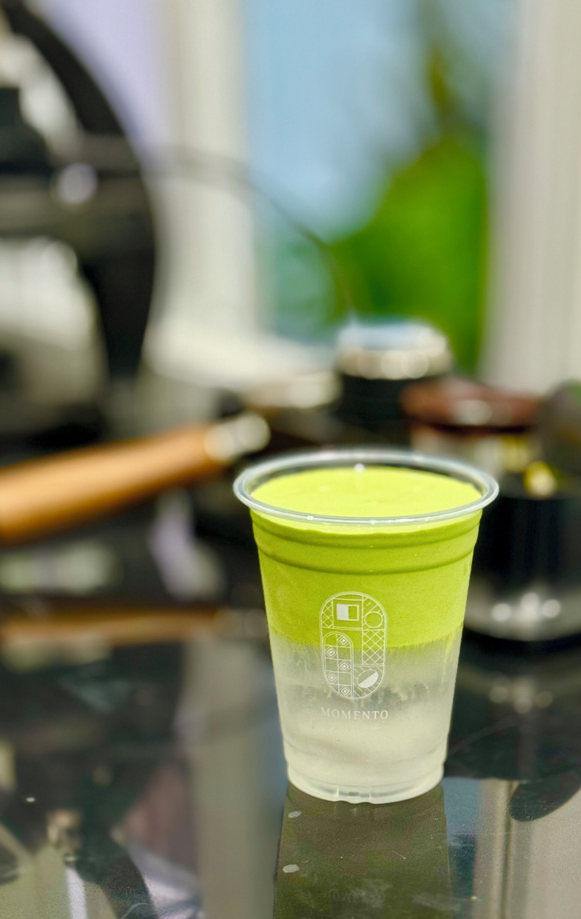 A clear plastic cup with a green liquid on a reflective surface.