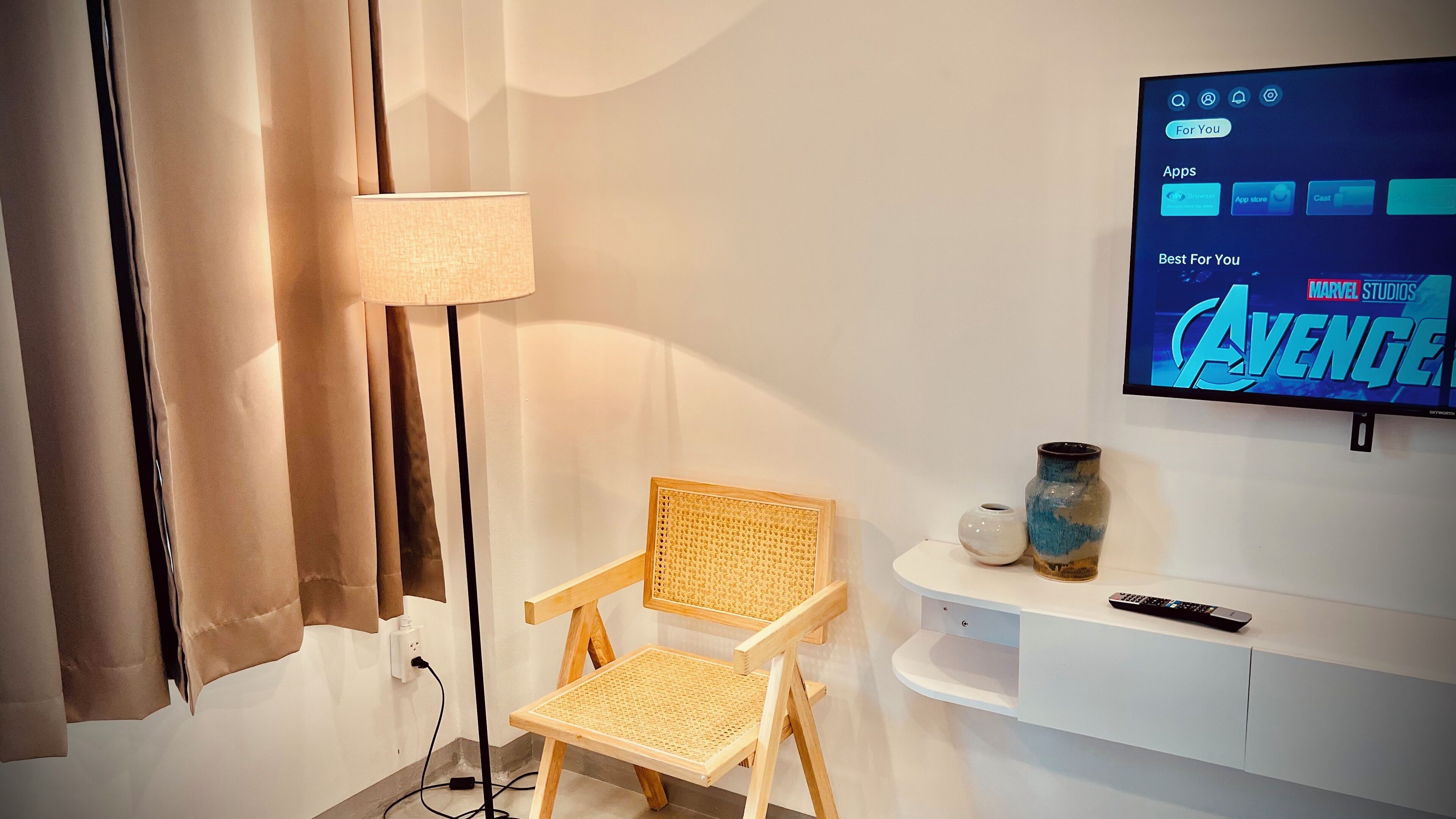 Une pièce avec un téléviseur diffusant le film « Avengers : La Bataille finale » des studios Marvel, une chaise en bois, un vase et une télécommande posés sur une console blanche.