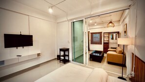 A modern hotel room with a large bed, a flat-screen TV mounted on the wall, a sliding glass door leading to a balcony, and a small table with a lamp. - Momento Hotel and Cafe (Khon Kaen)
