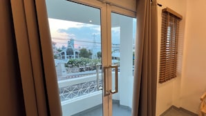 A view from a balcony with a glass door, a metal railing, and a window with blinds. - Momento Hotel and Cafe (Khon Kaen)