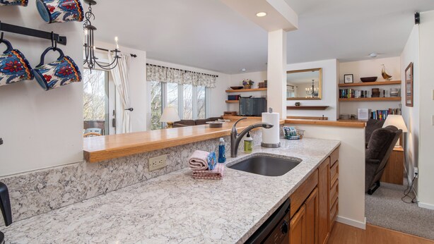 A modern kitchen with marble countertops, a sink, and wooden cabinets. There are decorative items on the shelves and a chandelier above the sink. - Cozy Sugarbush condo w/ ski-in/ski-out (Warren)