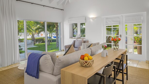A modern living room with a sofa, dining table, and chairs. There is a window with a view of a garden and a door leading outside. - Captian's Suite @ Yacht Club, Large Suite 5-minute walk from Grace Bay Beach (Providenciales)