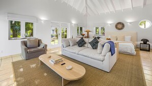 A modern living room with a white sofa, a grey armchair, and a wooden coffee table. There is a bed with white bedding and a round mirror on the wall. - Captian's Suite @ Yacht Club, Large Suite 5-minute walk from Grace Bay Beach (Providenciales)