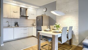 A modern kitchen with white cabinets, a stainless steel refrigerator, and a dining area with a table set for two. - Apartamenty Sun & Snow Blue Baltic (Pogorzelica)