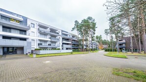 A modern apartment building with multiple balconies, a paved courtyard, and surrounding greenery. - Apartamenty Sun & Snow Blue Baltic (Pogorzelica)