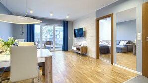 A modern living room with a wooden floor, a dining area with a white table, and a grey sofa. - Apartamenty Sun & Snow Blue Baltic (Pogorzelica)