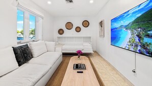 Ein modernes, helles Wohnzimmer mit einem weißen Sofa, einem Couchtisch und einem Flachbildfernseher, der einen schönen Ausblick auf einen Strand zeigt.