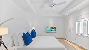 Une chambre moderne avec un grand lit, un ventilateur de plafond, un téléviseur fixé au mur et une fenêtre.